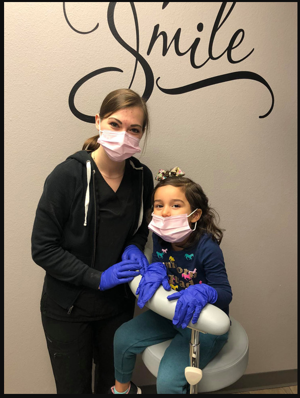 A Rose Dental Care team member with a young patient in front of the Smile wall